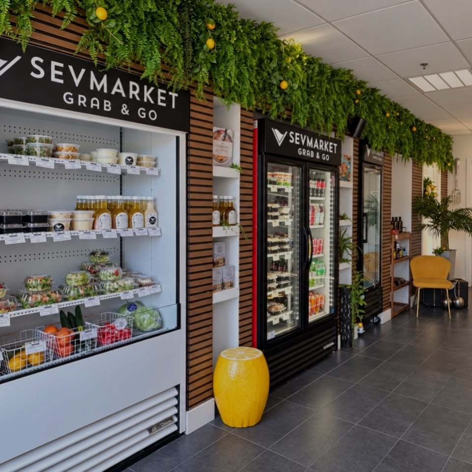 The Sevmarket Grab & Go wall of fridges under a greenery ceiling